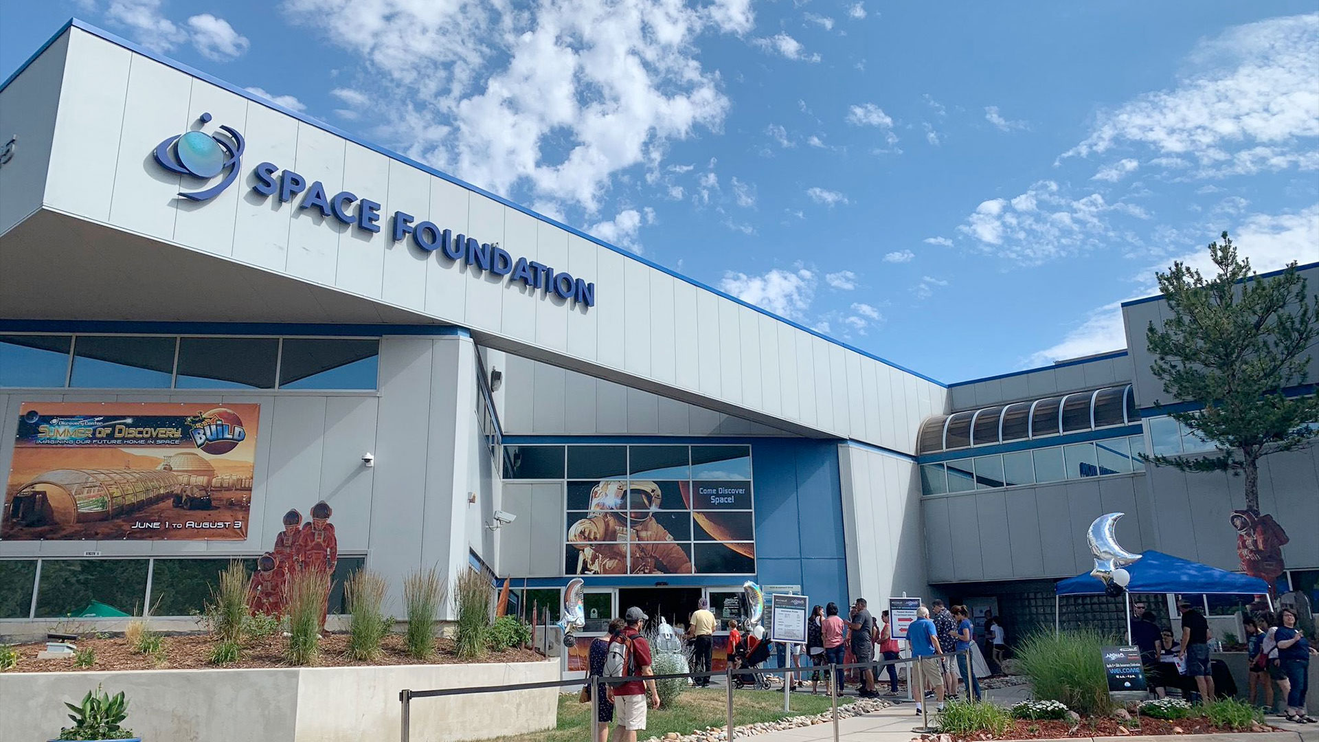 photo of a the outside of a white building with "space foundation" written on its wall in blue letters