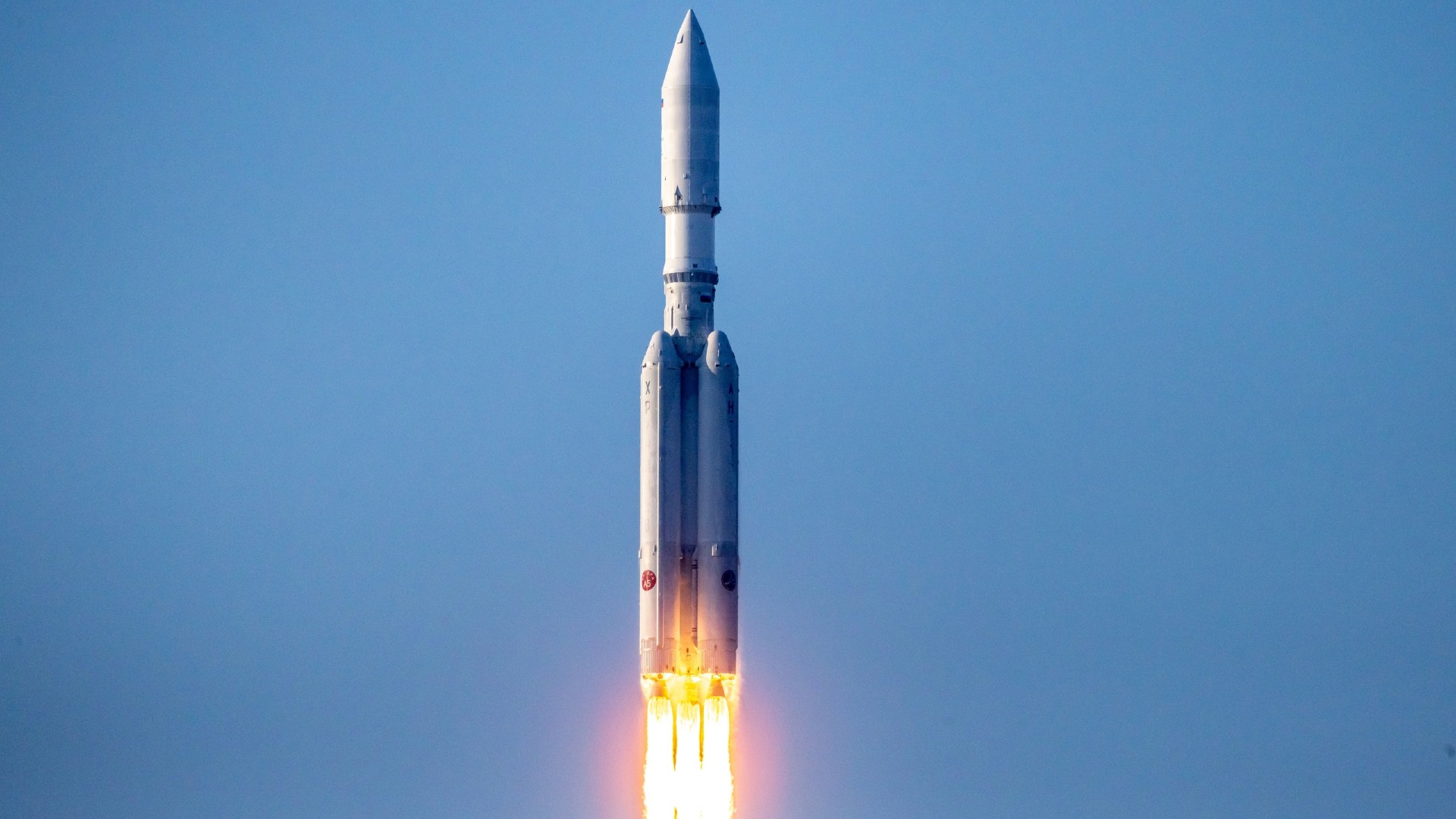 a large white rocket with four smaller boosters lifts off above a plume of fire