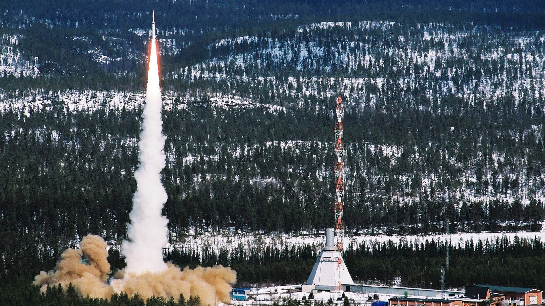 sounding rocket lifting off with a forest and snow in behind