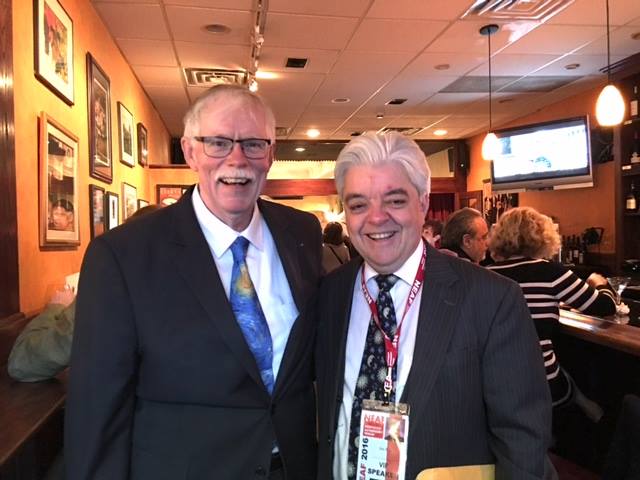 two men in suits smile for a photo