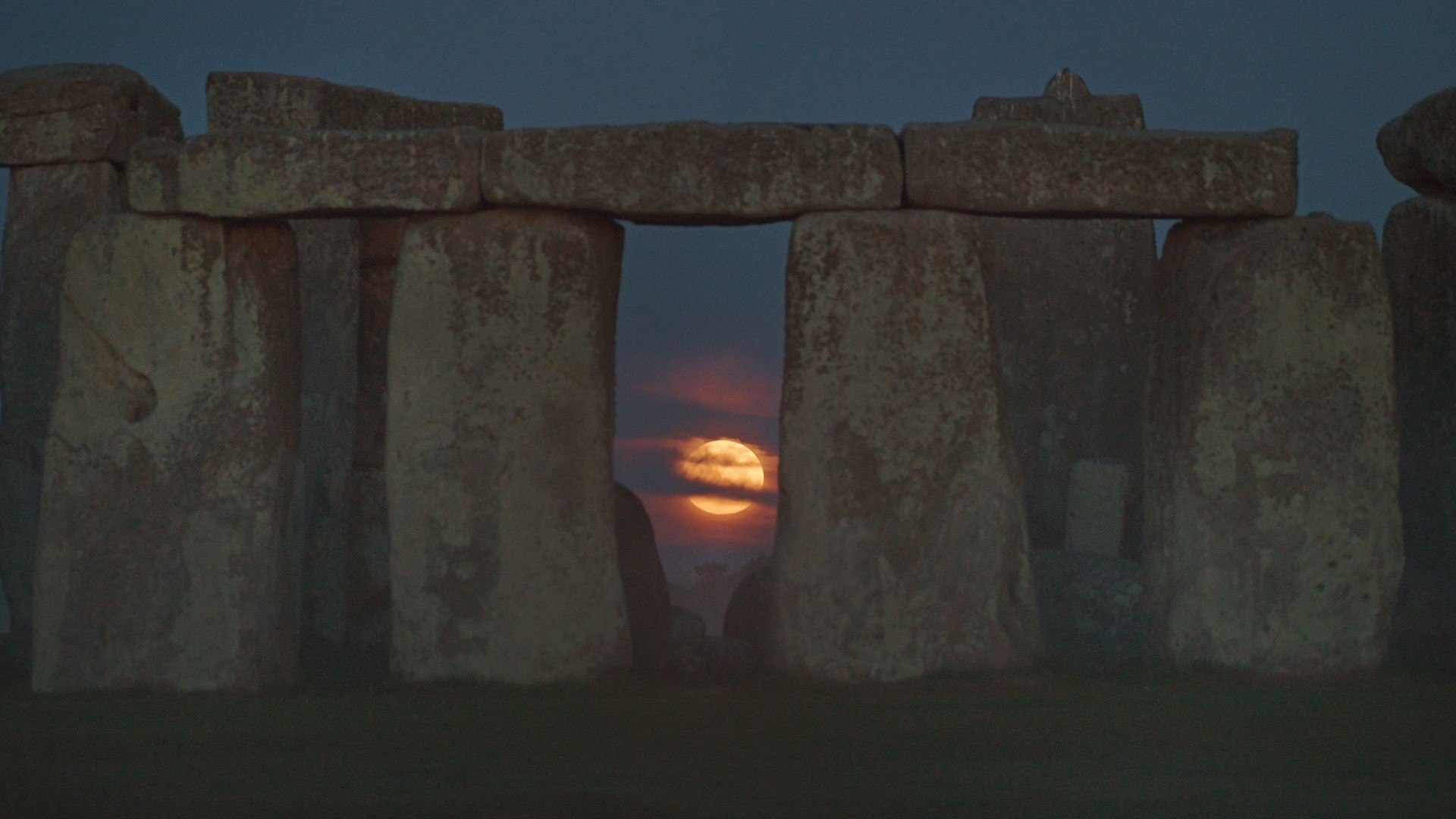 the full moon can be seen between large slabs of stone standing upright