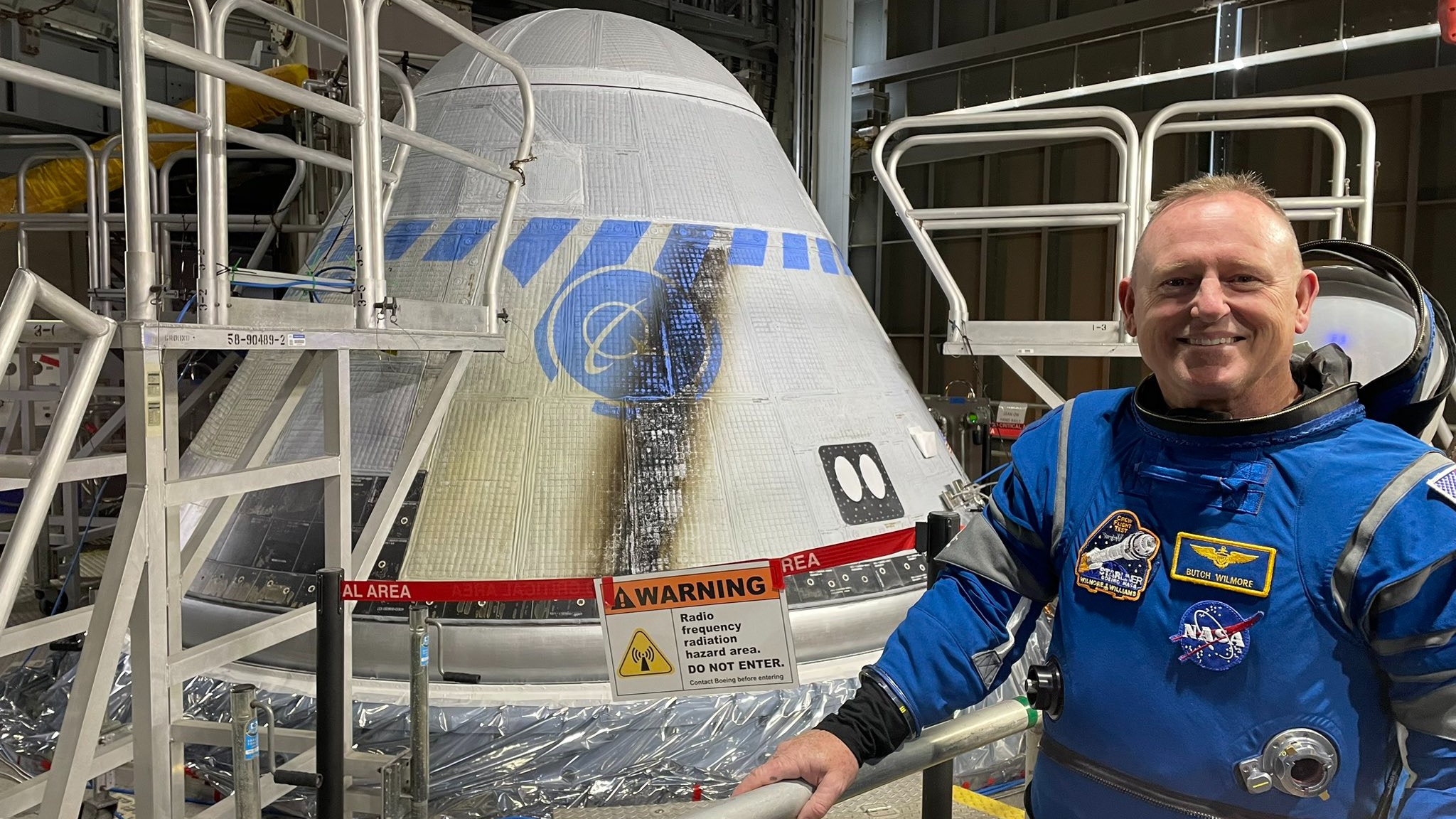 an astronaut in spacesuit next to a cone-shaped spacecraft in a facility